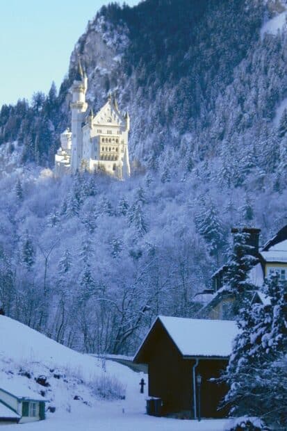 Neuschwanstein Castle shines brightly in the snowy forest near mountain slopes, HD Phone Wallpaper