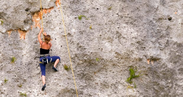 A woman is carefully ascending a rugged rock face using climbing gear and ropes, 2K Desktop Wallpaper