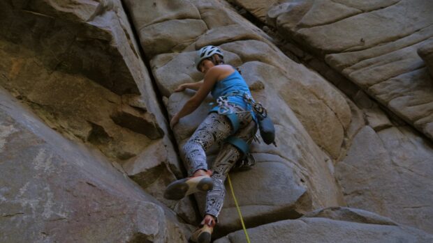 A woman wearing climbing gear ascends a rocky mountain wall with focus and determination, 4K Desktop Wallpaper