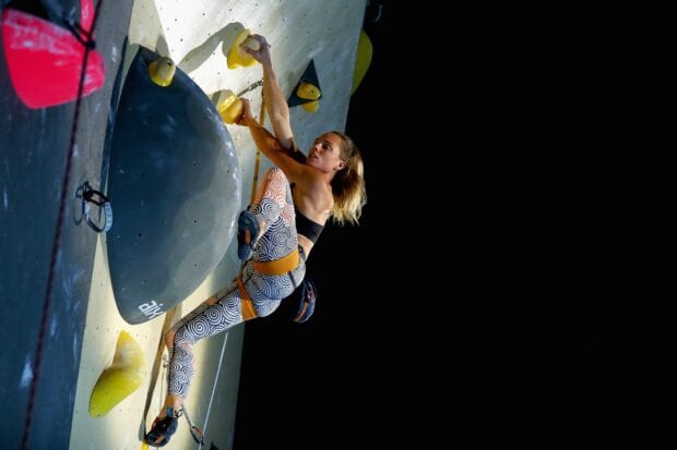 A woman is focused on rock climbing indoors with colorful grips on the climbing wall, 2K Desktop Wallpaper