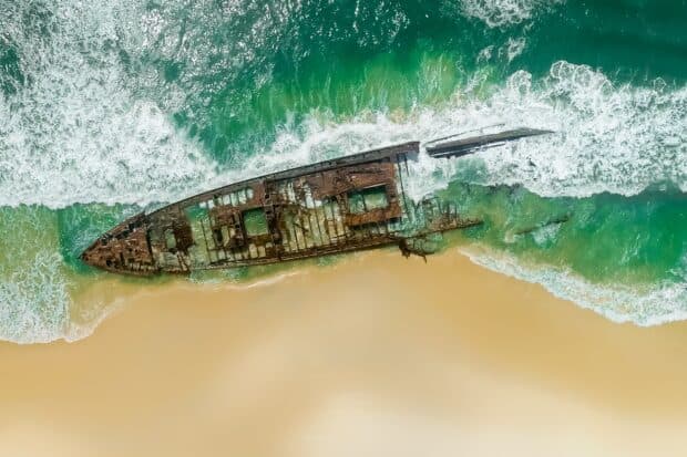 A rusted shipwreck lies on the sandy shore of Fraser Island as waves gently wash over it, HD Desktop Wallpaper