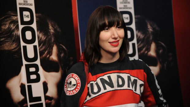 A woman wearing a colorful vintage jacket stands in front of movie posters at an event featuring Yeah Yeah Yeahs wallpapers, 2K Desktop Wallpaper