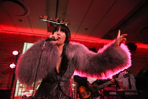The lead singer of Yeah Yeah Yeahs is passionately performing on stage with a microphone in hand, 2K Desktop Wallpaper