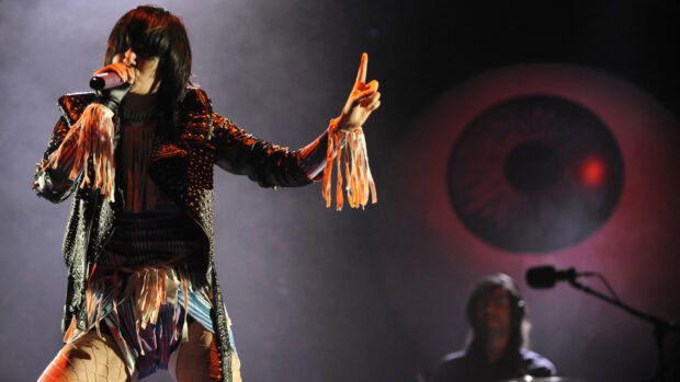 The lead singer of Yeah Yeah Yeahs is performing live with a microphone on stage, HD Desktop Wallpaper