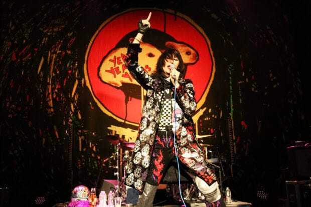 The lead singer of Yeah Yeah Yeahs is performing on stage with a red and black backdrop, HD Desktop Wallpaper