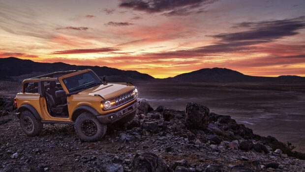 A yellow Ford Bronco is driving off road on rocky terrain during a colorful sunset, 4K Desktop Wallpaper