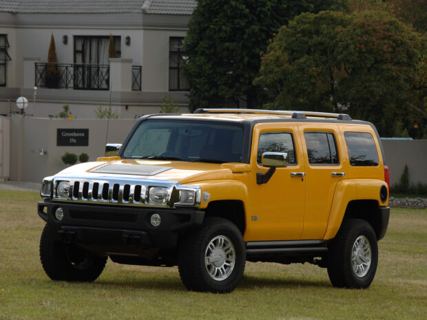 A yellow Hummer H3 is parked on grass near a residential area with trees and buildings, HD Desktop Wallpaper