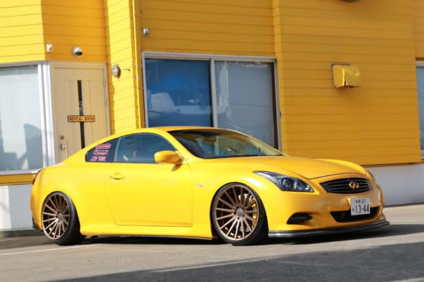 A yellow Infiniti G37 is parked near a yellow building showing custom wheels and modified details, 2K Desktop Wallpaper