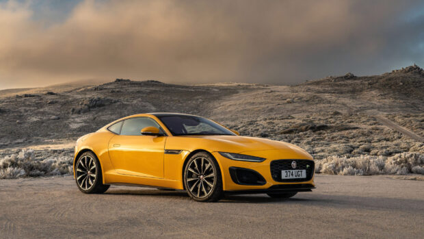 A yellow Jaguar F Type sports car is parked on a desert road under a cloudy sky, 2K Desktop Wallpaper