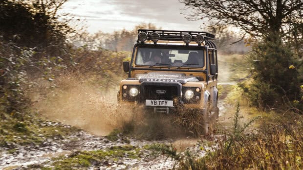 A yellow Land Rover Defender is splashing mud while driving off road on a forest trail, 4K Desktop Wallpaper