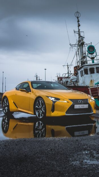 A yellow Lexus LC 500 is parked near fishing boats on a wet surface, 2K Mobile Wallpaper