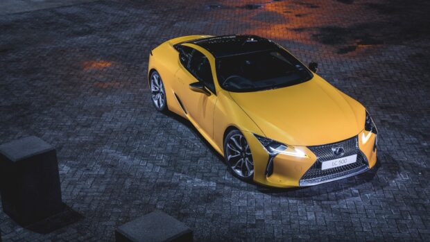 A yellow Lexus LC 500 sports car is parked on a paved surface at night showing its sleek design and headlights, 4K Desktop Wallpaper