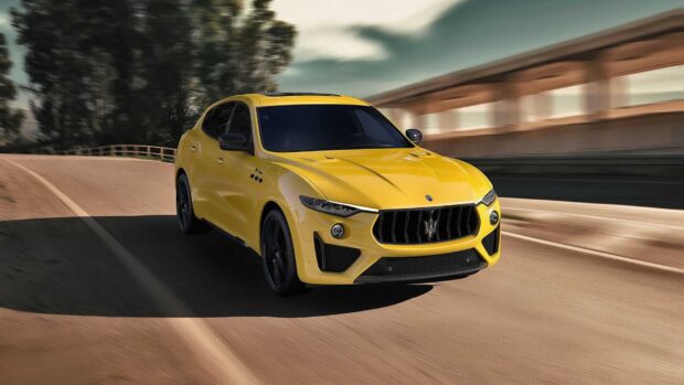 A yellow Maserati Levante is driving fast on a curvy road with trees and a bridge, HD Desktop Wallpaper