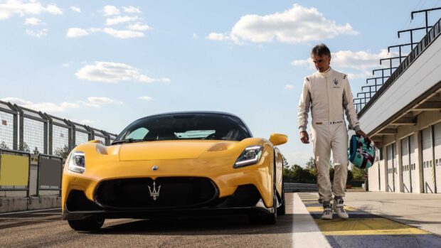A driver stands beside the yellow Maserati Mc20 on the race track holding a helmet, HD Desktop Wallpaper