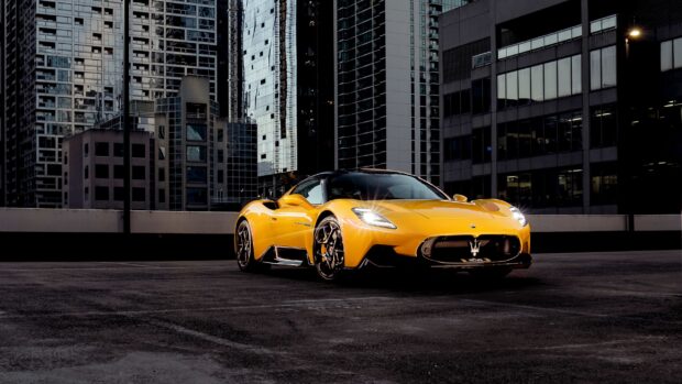 A yellow Maserati Mc20 is parked on a rooftop with city buildings in the background, 2K Desktop Wallpaper