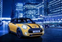 A yellow Mini Cooper is parked on a city street with illuminated buildings in the background, HD Desktop Wallpaper