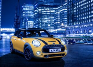 A yellow Mini Cooper is parked on a city street with illuminated buildings in the background, HD Desktop Wallpaper