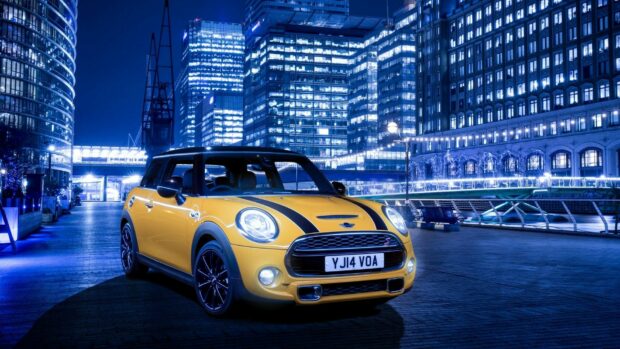 A yellow Mini Cooper is parked on a city street with illuminated buildings in the background, HD Desktop Wallpaper