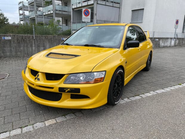 A yellow Mitsubishi Lancer Evo with black rims parked near a building on a paved street, HD Desktop Wallpaper