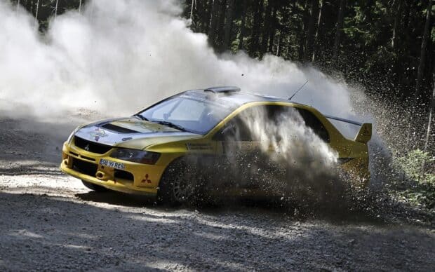A yellow Lancer Evo racing aggressively on a forest gravel track kicking up dust, HD Desktop Wallpaper