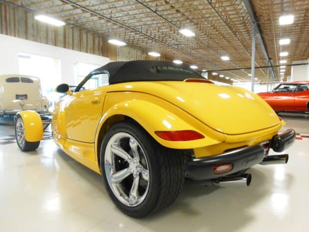 A yellow Plymouth Prowler is displayed indoors with other classic cars in the background, HD Desktop Wallpaper