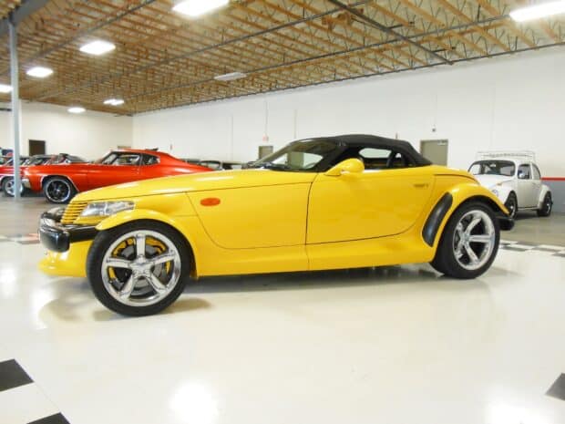A yellow Plymouth Prowler is parked indoors alongside other classic cars in a showroom, HD Desktop Wallpaper