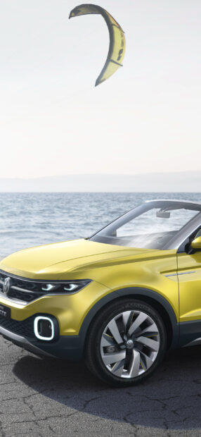 A yellow Volkswagen T Cross parked near the ocean with a kite in the sky above, 2K Phone Wallpaper