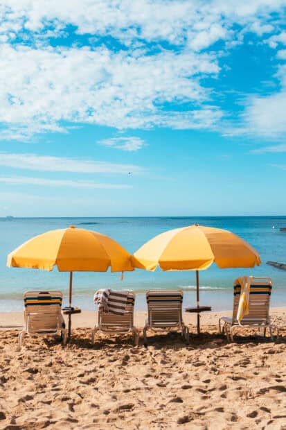 Four yellow beach umbrellas with chairs on the sandy shore under a blue sky, 2K Mobile Wallpaper