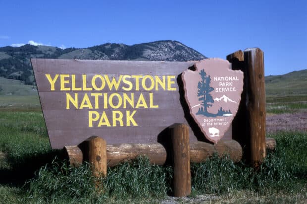 A wooden Yellowstone National Park sign stands with mountains in the background, HD Desktop Wallpaper
