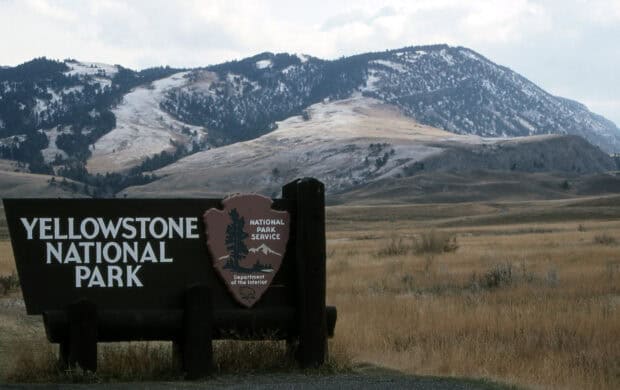 The Yellowstone National Park entrance sign stands in a field with mountains in the background, HD Desktop Wallpaper