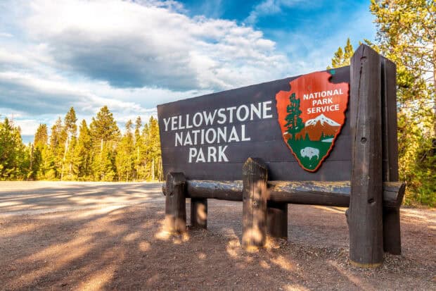 A wooden sign welcomes visitors to Yellowstone National Park surrounded by trees, 2K Desktop Wallpaper
