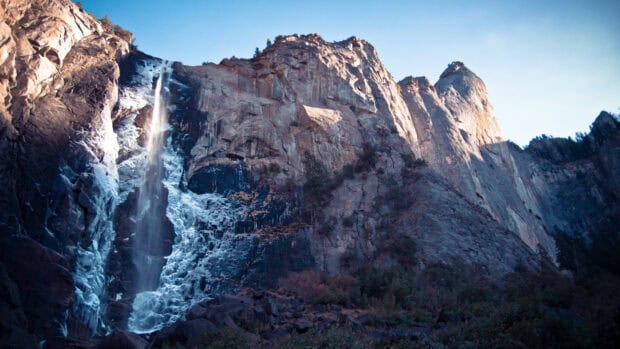 A tall waterfall cascades down rocky cliffs in Yellowstone National Park, 4K Desktop Wallpaper