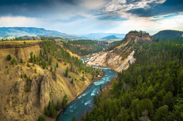 A clear river flows through rugged cliffs and forest in Yellowstone National Park, 2K Desktop Wallpaper