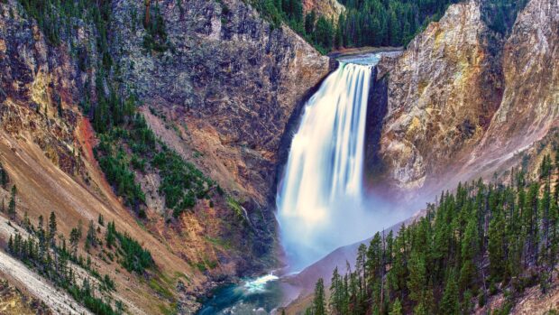 A stunning waterfall flowing through Yellowstone National Park surrounded by rocky cliffs and green trees, 4K Desktop Wallpaper
