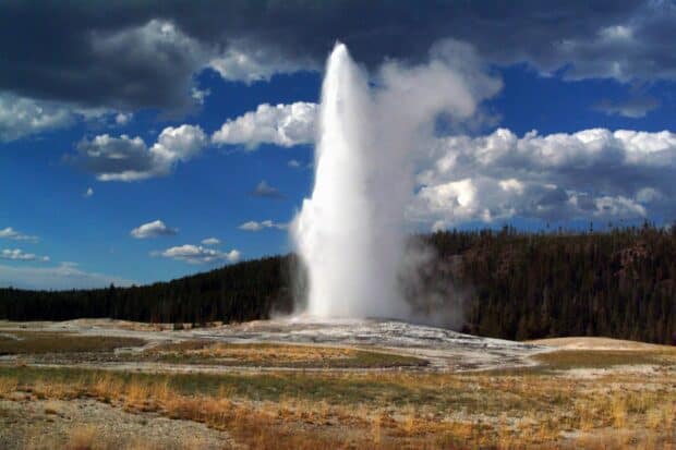 A geyser erupting with steam and water in Yellowstone National Park under a cloudy sky, HD Desktop Wallpaper