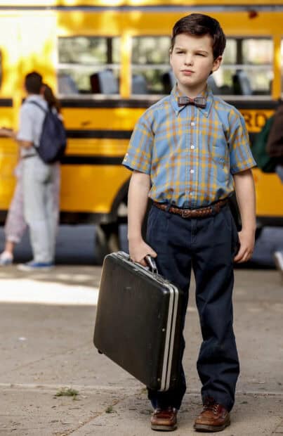 A young boy from Young Sheldon Tv Series is standing in front of a school bus holding a briefcase, 2K Mobile Wallpaper