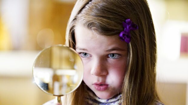 A young girl studies an object carefully using a magnifying glass in Young Sheldon Tv Series Wallpapers, HD Desktop Wallpaper