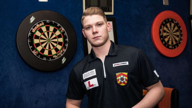 A young man stands confidently beside dartboards in a game room with darts wallpapers, HD Desktop Wallpaper