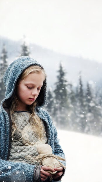 A young girl in a blue hooded coat is holding a doll while standing in a snowy forest, 4K Phone Wallpaper