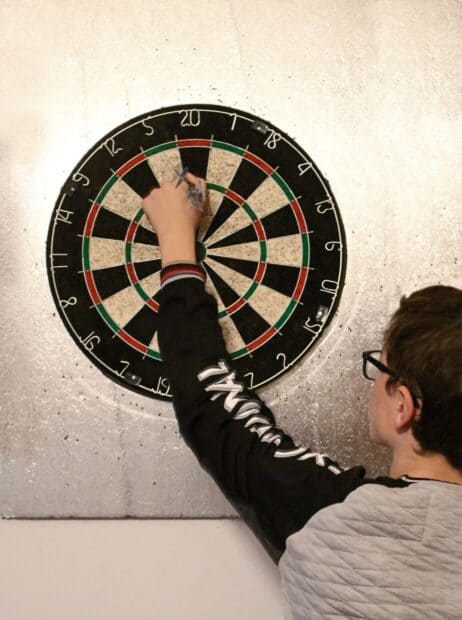 A young person is placing darts on a dartboard while focused on the game with darts wallpapers, HD Mobile Wallpaper