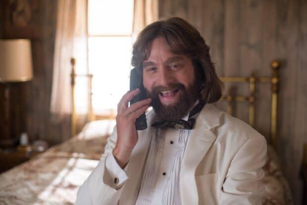 Zach Galifianakis is smiling while talking on a phone in a cozy room, 2K Desktop Wallpaper