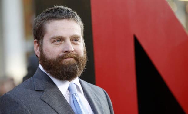 Zach Galifianakis is wearing a suit and light blue tie in front of a red and black background, 2K Desktop Wallpaper