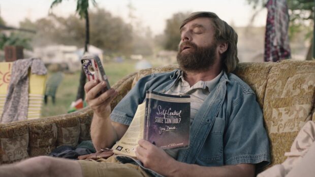 Zach Galifianakis is resting on a couch while holding a book and a phone outside, HD Desktop Wallpaper