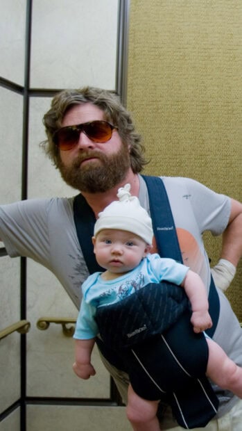 Zach Galifianakis is carrying a baby in a front carrier while wearing sunglasses, HD Mobile Wallpaper