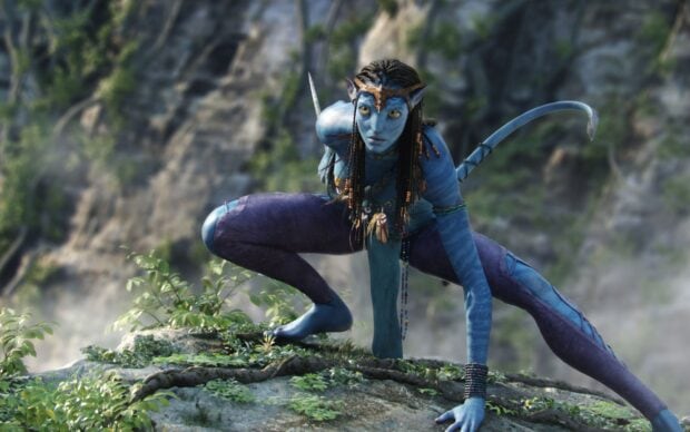 Zoe Saldana in Avatar crouches on a rocky ledge with detailed blue skin and braided hair, 2K Desktop Wallpaper