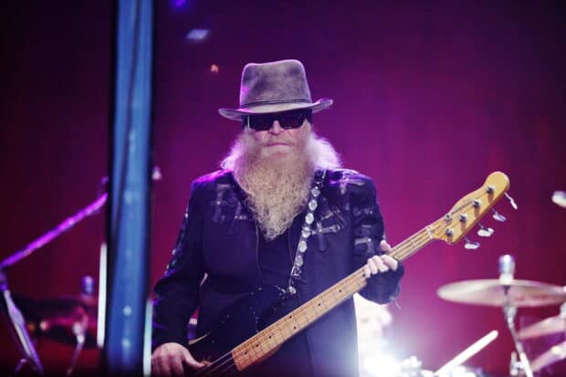 A Zz Top musician with a long beard and hat is playing a bass guitar with purple stage lights, 2K Desktop Wallpaper