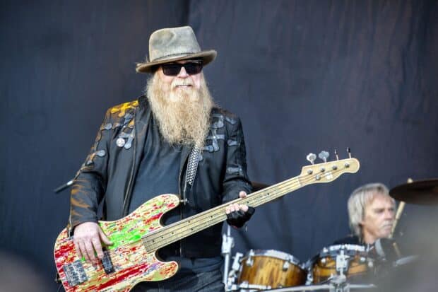 A Zz Top musician is playing a colorful bass guitar on stage during a live performance, 2K Desktop Wallpaper
