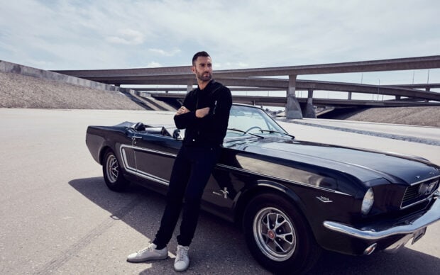 Adam Levine stands next to a black classic Mustang under an overpass, HD Desktop Wallpaper