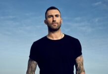 Adam Levine stands outdoors with a blue sky background showing his tattooed arms, HD Desktop Wallpaper