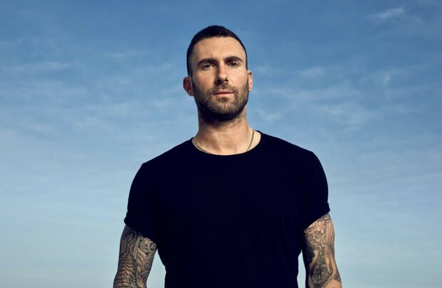 Adam Levine stands outdoors with a blue sky background showing his tattooed arms, HD Desktop Wallpaper